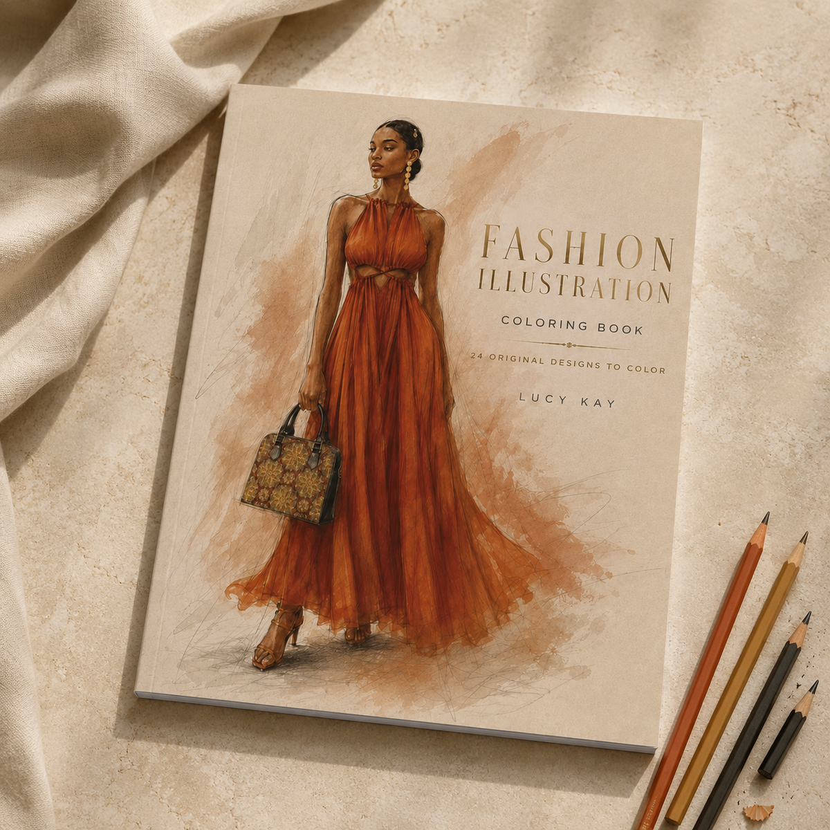 A fashion illustration coloring book titled 'Fashion Illustration Coloring Book' by Lucy Kay, featuring a watercolor-style drawing of a woman in a flowing rust-orange dress. The book is displayed on a textured beige surface with draped cream fabric and colored pencils nearby.