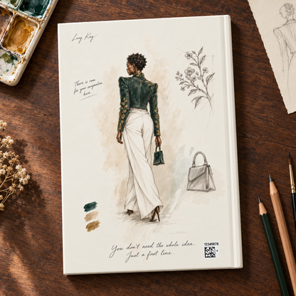 A hardcover sketchbook featuring an elegant fashion illustration of a woman in a dark green and gold patterned top with white trousers, shown on a dark wooden desk surrounded by art supplies.